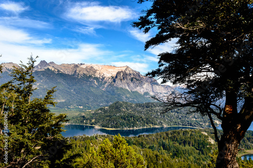 Beautiful lake landscape in the middle of mountains surrounded by pine trees and rocks everywhere. Very sunny day in the mountain of Bariloche. Green foliage and huge rocks. © Rariel