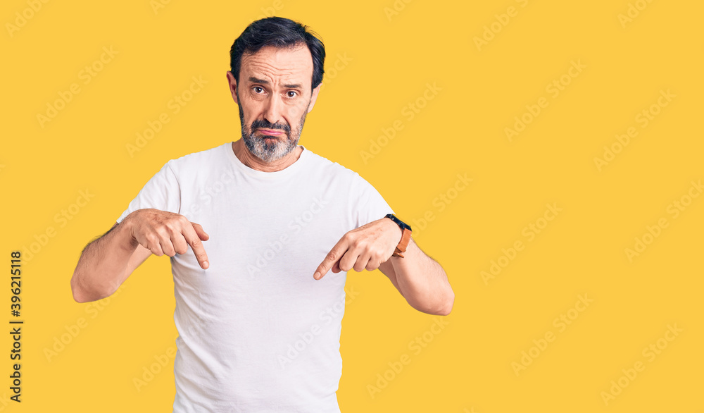 Middle age handsome man wearing casual t-shirt pointing down looking sad and upset, indicating direction with fingers, unhappy and depressed. Middle age handsome man wearing casual t-shirt pointing down looking sad and upset, indicating direction with fingers, unhappy and depressed.