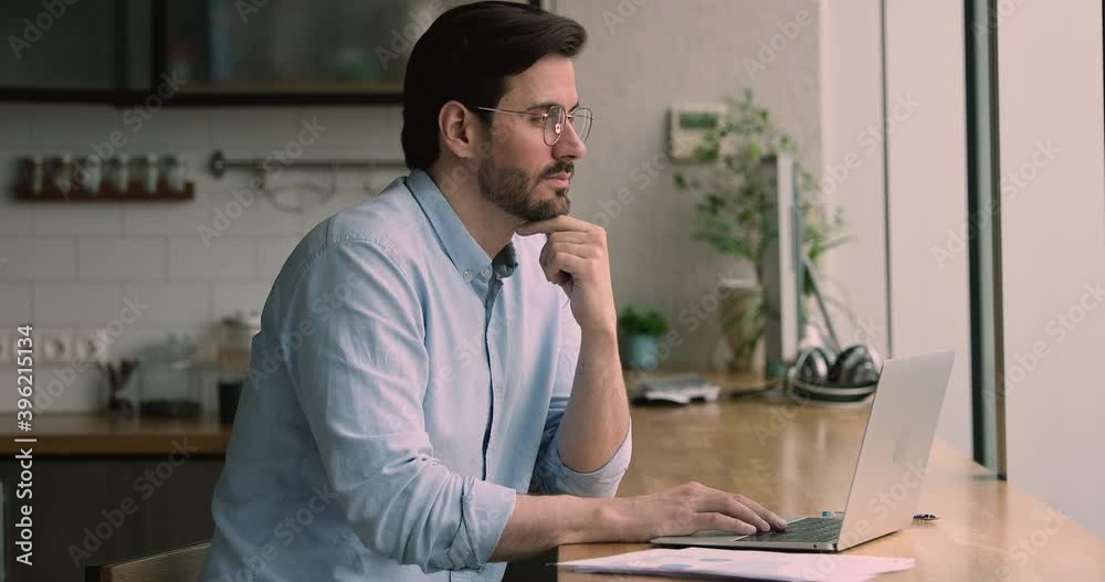 Serious businessman company ceo working from home due covid, sit in domestic kitchen at table using laptop device preparing financial report, solving issues, doing research, make financial data review