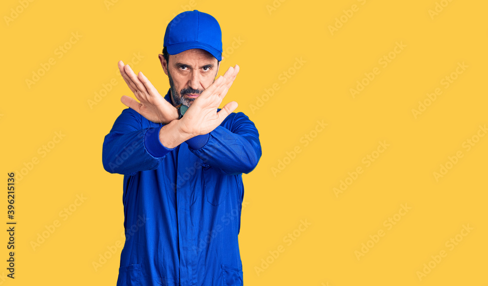 Middle age handsome man wearing mechanic uniform rejection expression crossing arms and palms doing negative sign, angry face
