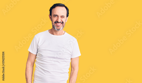 Middle age handsome man wearing casual t-shirt winking looking at the camera with sexy expression, cheerful and happy face.