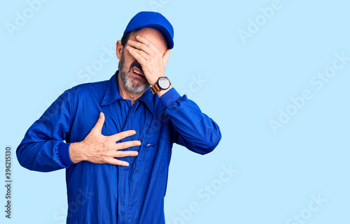 Middle age handsome man wearing mechanic uniform touching forehead for illness and fever, flu and cold, virus sick