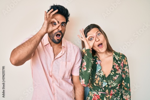 Beautiful young couple of boyfriend and girlfriend together doing ok gesture shocked with surprised face, eye looking through fingers. unbelieving expression.