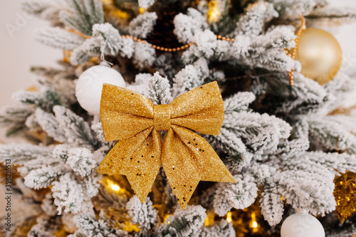 large gold shiny bow on Christmas tree in gold color. process of home decorating , selective focus