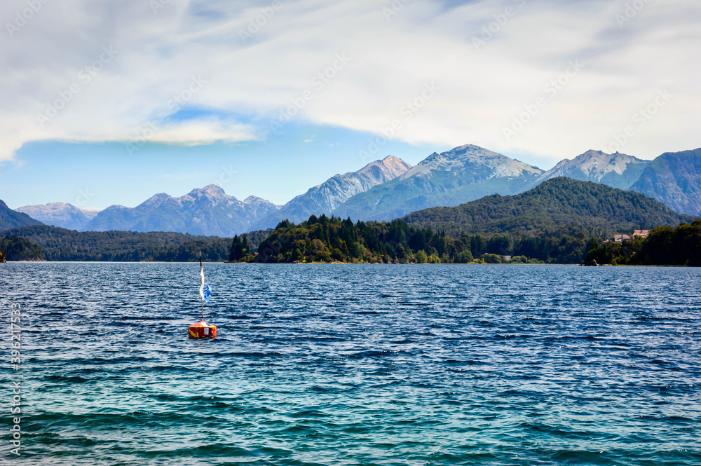 Beautiful scenery of a buoy floating on the lake surrounded by mountains, pine trees and rocks. Very sunny day in a rocky beach landscape.
