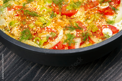cooked fried omelet with herbs, spices and vegetables in a black pan on a wooden table