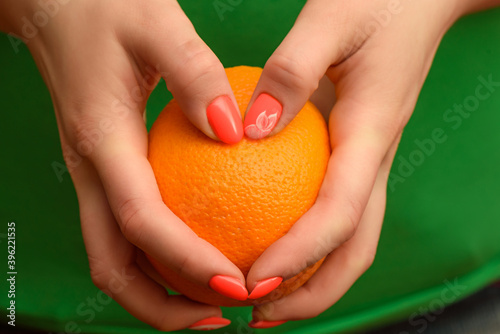 A girl with a beautiful orange manicure is holding a ripe orange in her hands. Close-up photo.