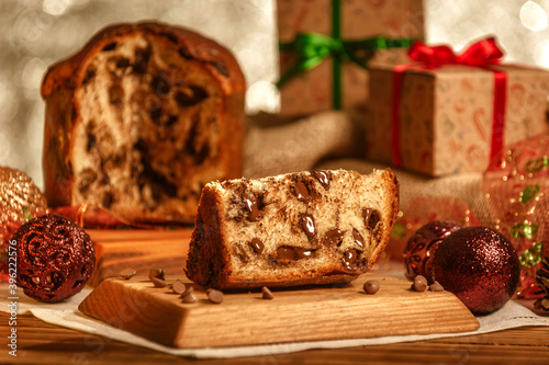 Slice of chocolate panettone  on wooden cutting board with christmas ornaments