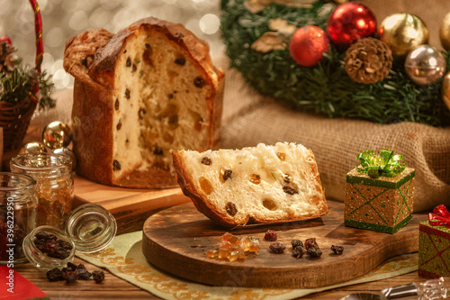 A slice of panettone and candied fruit cubes on wooden cutting board with christmas ornaments