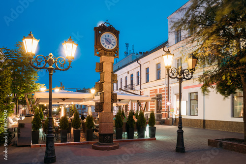 Brest, Belarus. Two-Sided Clock With Arms Of City Of Different Times In Form Of Six-Meter Bronze Monument On Pedestrian Sovietskaya Street In Evening Night Illuminations.