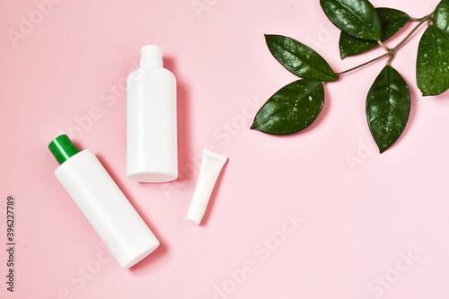 White blank tubes with cosmetics products on pink background. Cream tube  moisturizing foam and tonic water and green plant. Professional skincare concept.