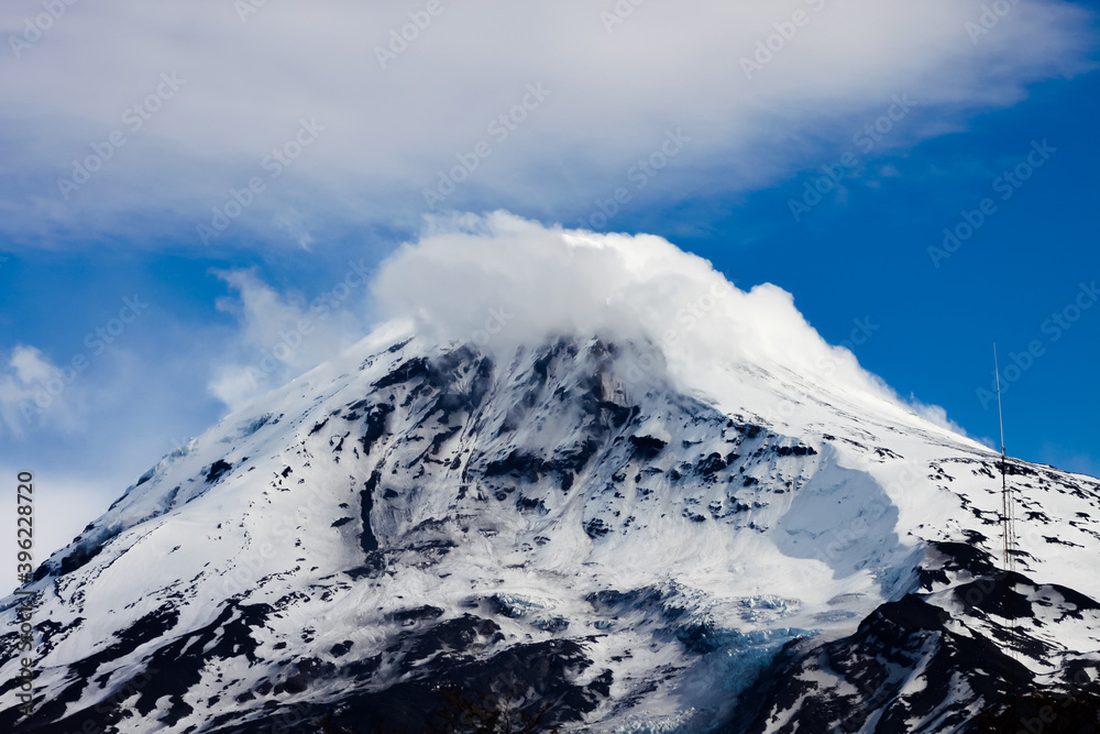 Top of the Lanin Volcano from Lake Tromen in Neuquen, Argentina. This volcano is covered by eternal snow and with some clouds that surround the caldera of the volcano.