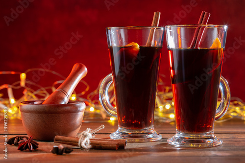 Two glasses of christmas mulled wine with spices on wooden table against illumination light.