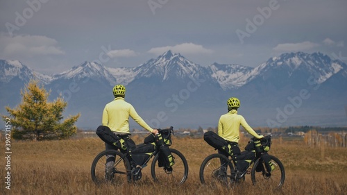 The man and woman travel on mixed terrain cycle touring with bikepacking. The two people journey with bicycle bags. Mountain snow capped.