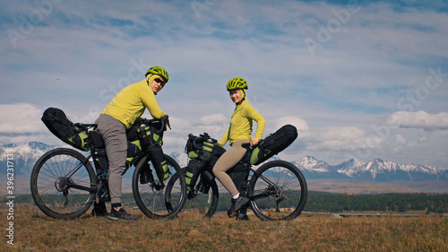 The man and woman travel on mixed terrain cycle touring with bikepacking. The love couple journey with tent in with bicycle bags. Stylish sportswear.