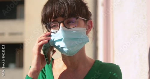 Brunette woman, wearing glasses, makes a phone call with a mask during lockdown photo