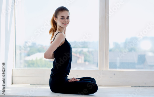 Free Download Woman practices yoga and hands behind her back crossed legs by window room - GFXLoad