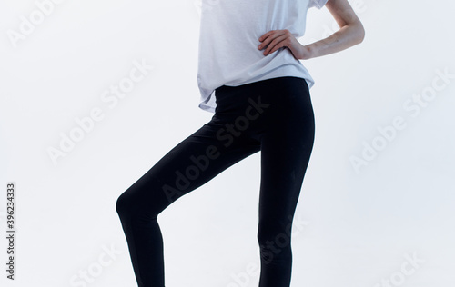 Cropped view of a woman in a white t-shirt and black leggings on a light background © SHOTPRIME STUDIO