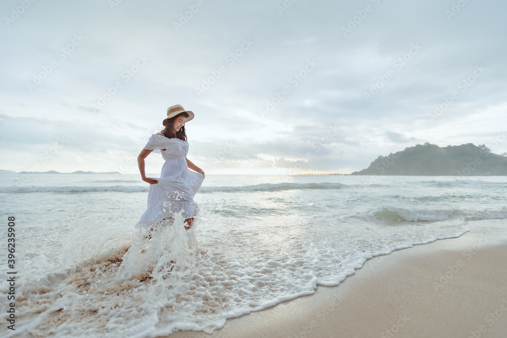 Asian woman wearing stylish hat and clothes walking on the beach and enjoying beautiful nature in the sunset time. Summer holidays and travel concept. Asian woman wearing stylish hat and clothes walking on the beach and enjoying beautiful nature in the sunset time. Summer holidays and travel concept.