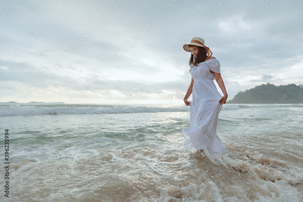 Asian woman wearing stylish hat and clothes walking on the beach and enjoying beautiful nature in the sunset time. Summer holidays and travel concept. Asian woman wearing stylish hat and clothes walking on the beach and enjoying beautiful nature in the sunset time. Summer holidays and travel concept.
