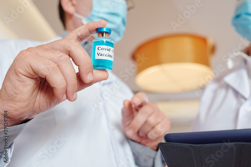 Close-up image of researcher showing vial with coronavirus vaccine at meeting with colleague