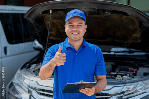 A young Asian auto mechanic opens the bonnet. To check for engine damage And perform professional maintenance. He wearing blue uniform.