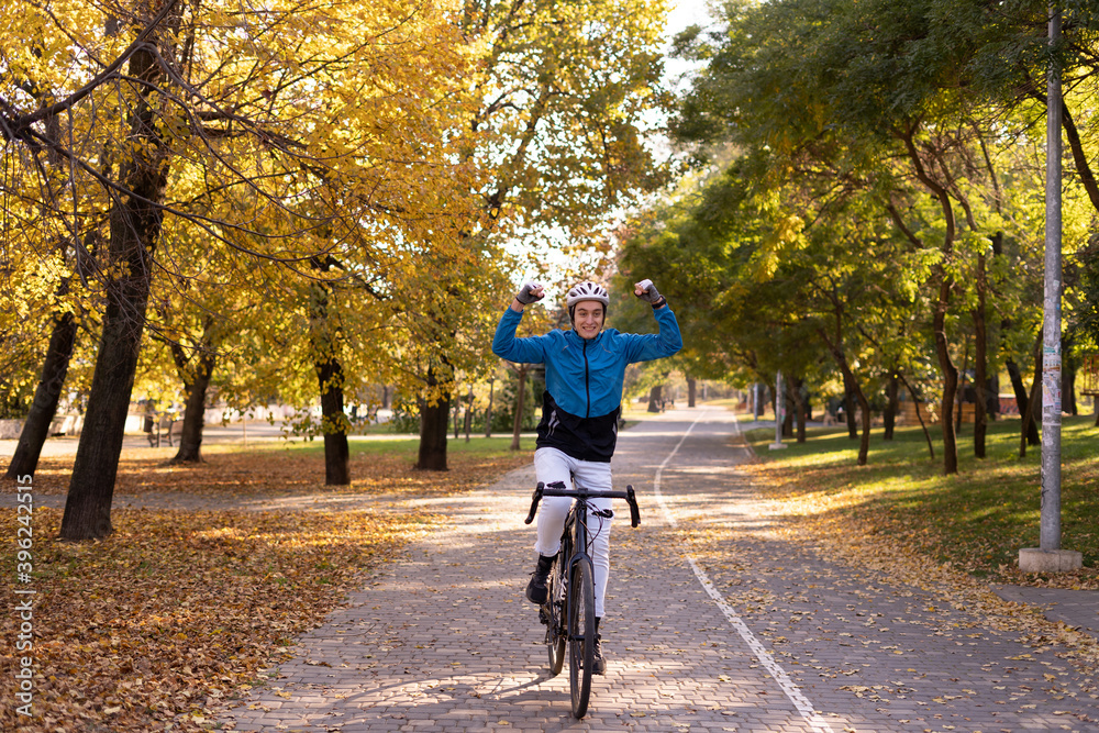 A young man rides a bicycle in the park with his hands up. Sportsman in helmet and suit.