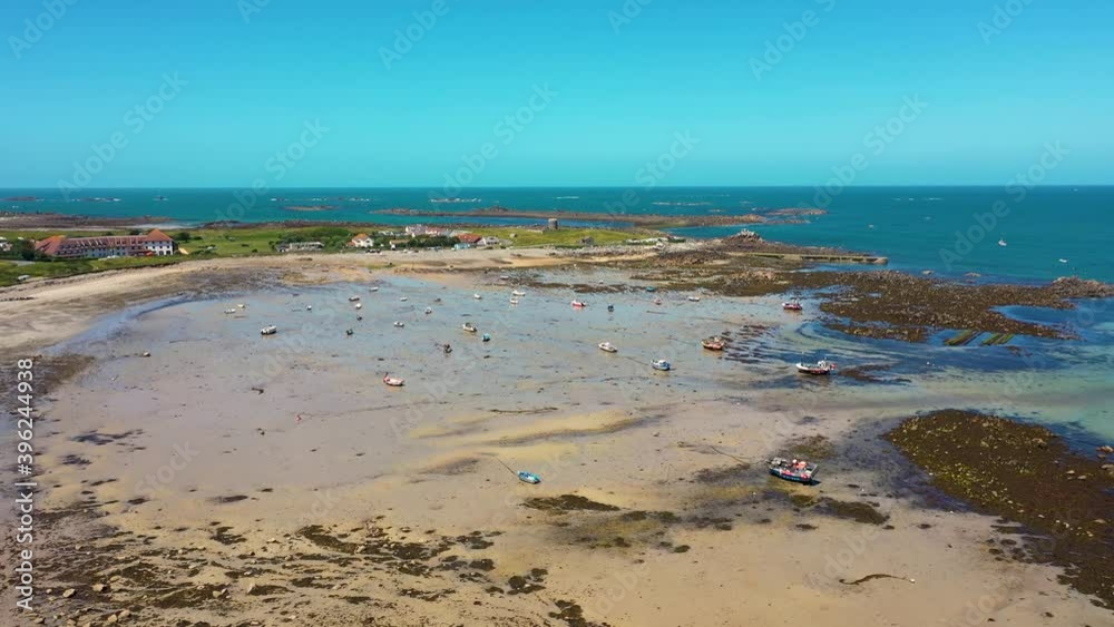 Flight over north Guernsey natural bay with drying boats on a summer day with sandy beach and Martello Tower and sea in the background Flight over north Guernsey natural bay with drying boats on a summer day with sandy beach and Martello Tower and sea in the background