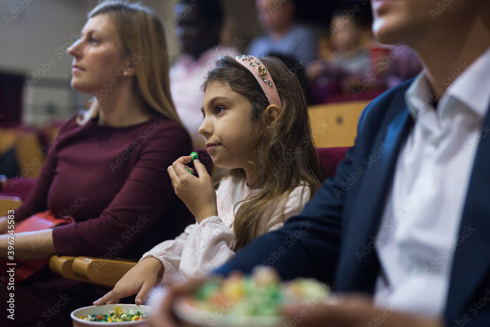 Fototapeta premium Family with child eating popcorn and watching a movie in the cinema