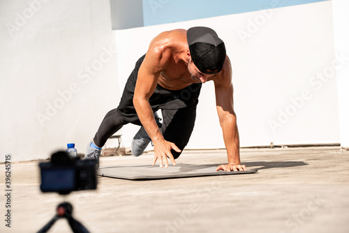 Male fitness influencer recording ourdoor home exercise video clip with camera on rooftop photo