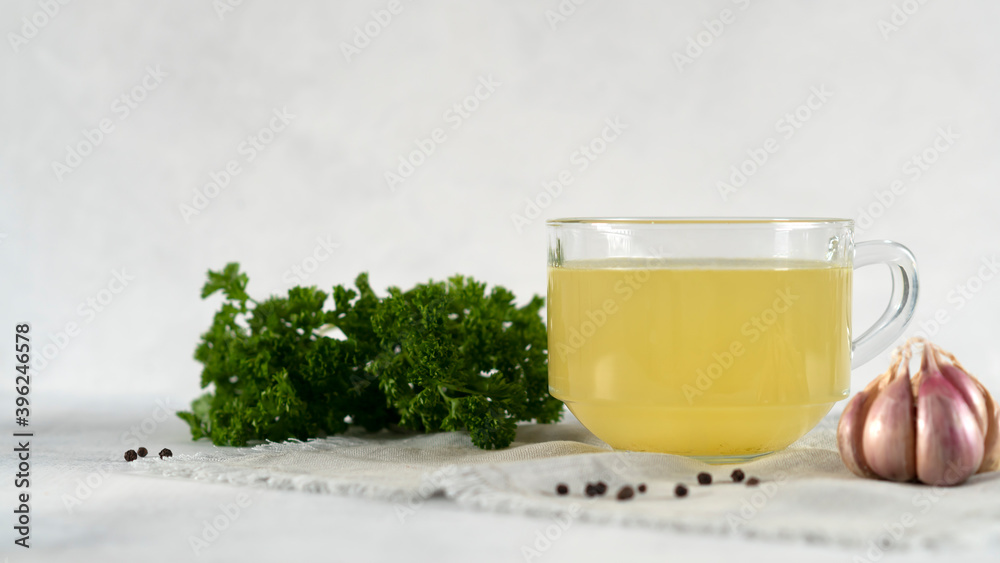 Homemade turkey bone broth in glass cup with parsley, peppercorns and