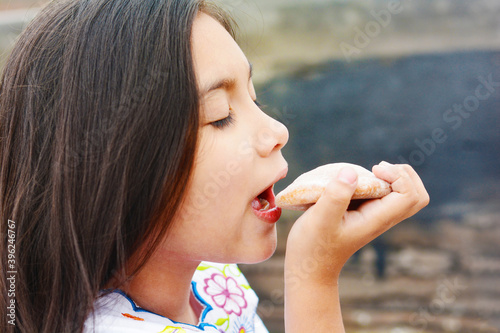 Happy latin little girl eating traditional bun. photo