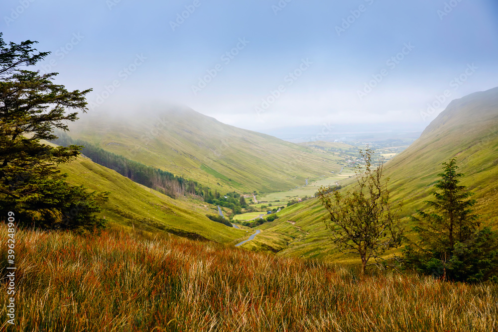 Rugged landscape at Glengesh Pass, County Donegal, Ireland. Beach with cliffs, green rocky land with sheep on foggy cloudy day. Wild Atlantic Way region.