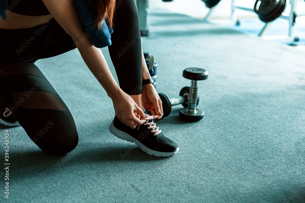 woman's hands tying shoelaces on sport sneakers in gym. dumbbell and water bottle on the ground around the sport girl.