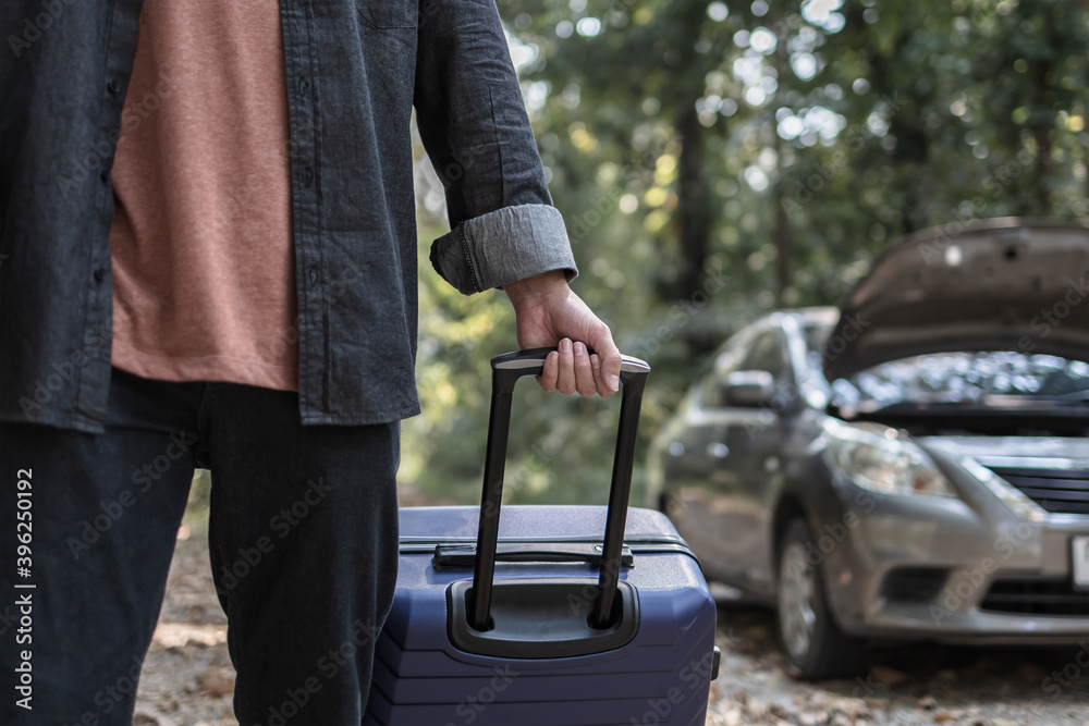 Obraz premium Man' hand drag to travel bag in front of open hood of a broken car on the road in the forest. Car breakdown concept.