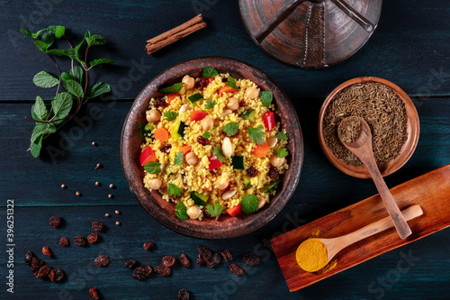 Traditional couscous in a tajine, shot from the top with spices and herbs on a dark wooden background photo