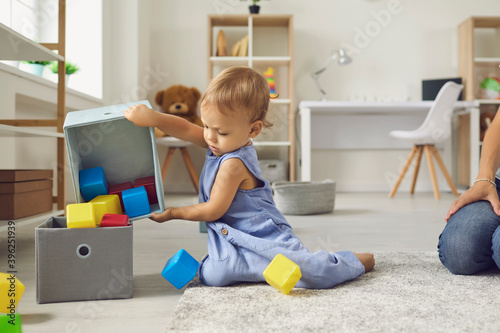 Cute little 2 year old child putting toys back in their place, helping mommy to tidy up photo