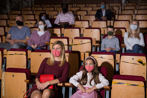Mom and daughter in protective masks in auditorium watching play in the theater. High quality photo