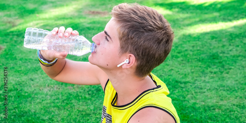 Thirsty athlete drinking water after workout. Young man, teen drink clear blue water from a plastic bottle after workout