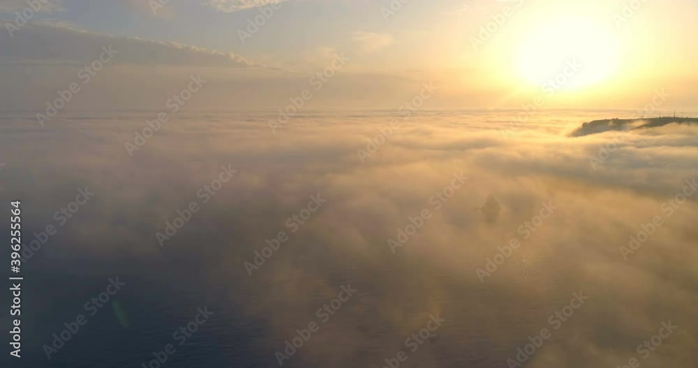 Moving white clouds orange sky scenic aerial view. Drone flies high back in orange sky through the fluffy clouds in the evening at the bright sun. Sun is hidden behind the clouds at sunset the fog. Moving white clouds orange sky scenic aerial view. Drone flies high back in orange sky through the fluffy clouds in the evening at the bright sun. Sun is hidden behind the clouds at sunset the fog.