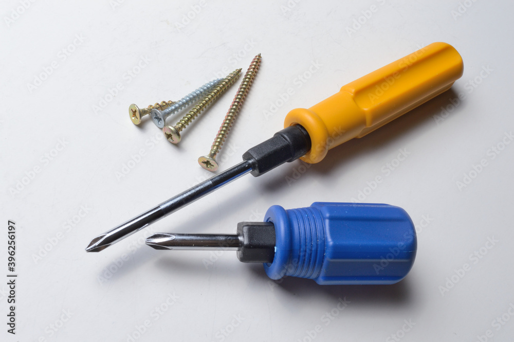 two different screwdrivers and several screws on a white background. close-up. two different screwdrivers and several screws on a white background. close-up.