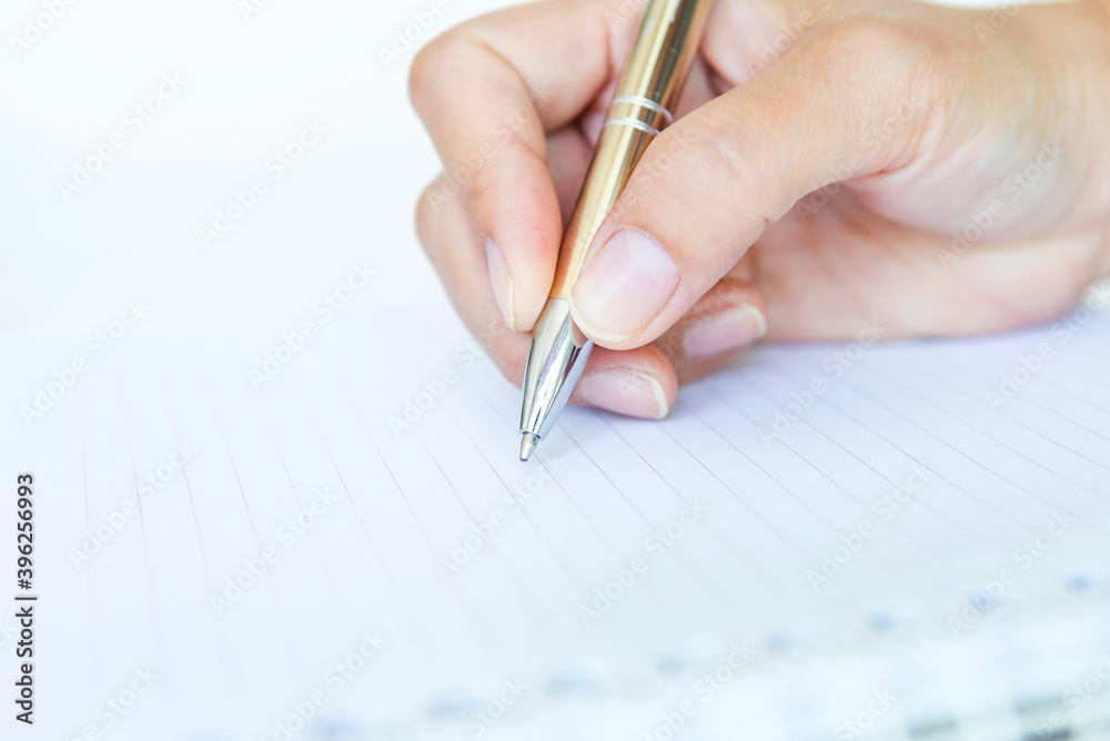 Hand holding silver pen on blank white note book, business project and signing contract, business and education concept Hand holding silver pen on blank white note book, business project and signing contract, business and education concept