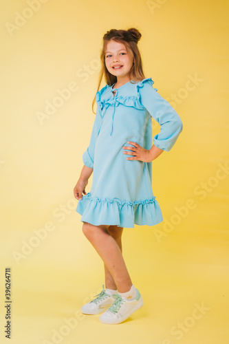 Teenage girl in a blue dress on a yellow background. Fashionable child. Studio photo