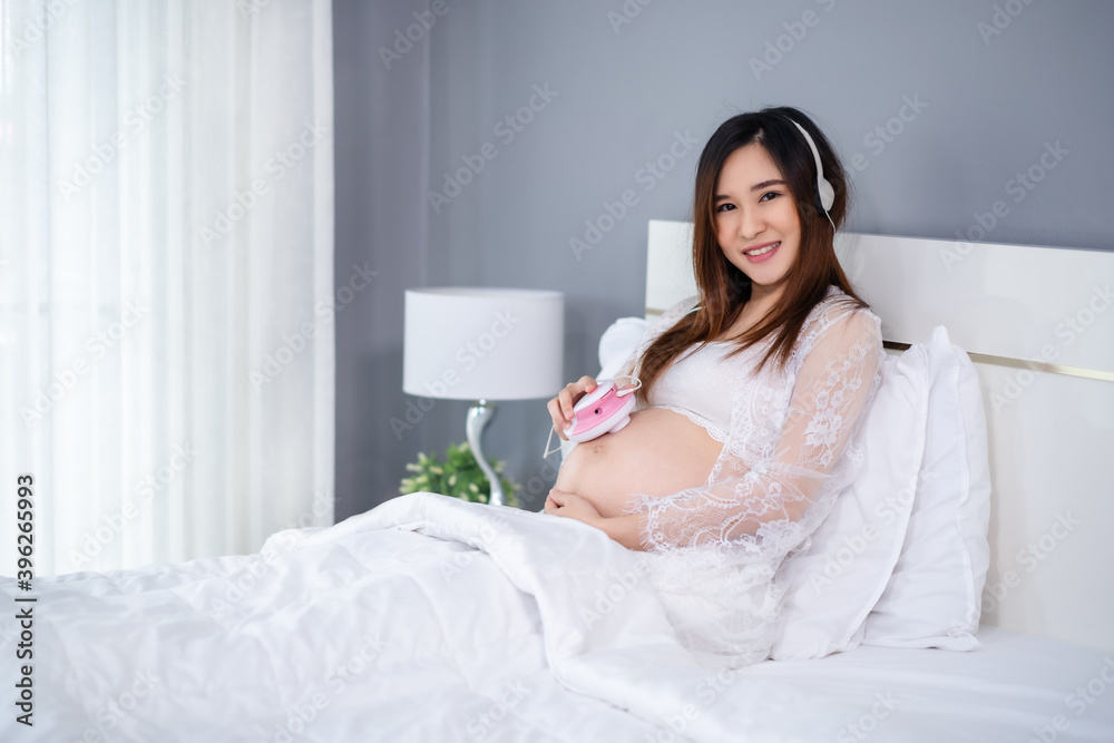 pregnant woman listening to fetal heart sound through headphones on bed