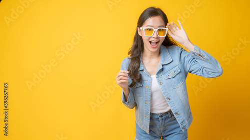 young cute Asian woman wearing yellow fashion glasses in jeans posing and smiled, Thai joyful and beautiful girl isolated on yellow background
