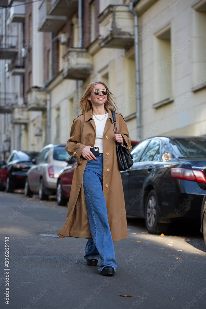 Young woman in a fashionable long coat walks in autumn city. copy space
