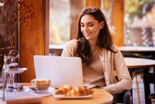 Attractive young woman using her laptop while sitting in the cafe near the window