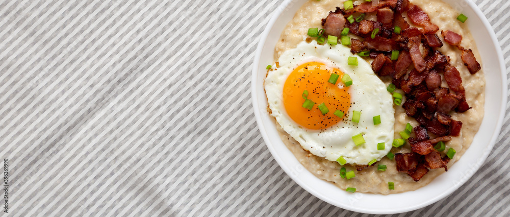 Homemade Cheesy Bacon Savory Oatmeal Bowl on cloth, view from above. Top view, overhead, flat lay. Copy space.