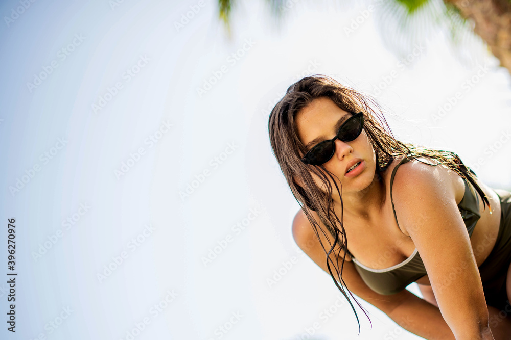 cute young teenage girl or woman posing and having fun on the beach under palm trees in summer swimsuit . Trendy girl posing. Funny and positive woman in sunglasses cute young teenage girl or woman posing and having fun on the beach under palm trees in summer swimsuit . Trendy girl posing. Funny and positive woman in sunglasses