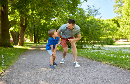 family, fatherhood and people concept - happy father and little son compete in running at summer park
